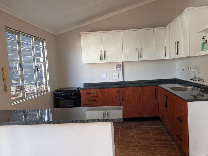 A clean, functional kitchen featuring granite countertops, two-tone cabinetry, tiled flooring, and a freestanding stove, offering a practical layout for daily use.