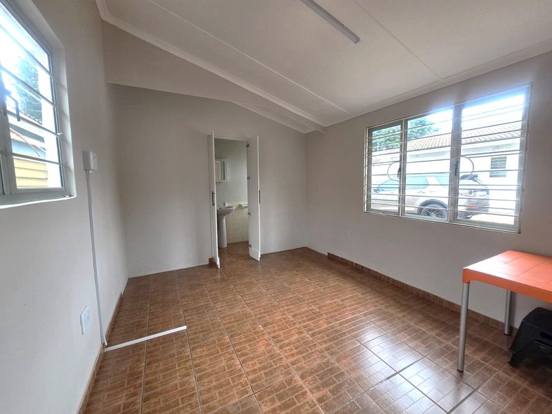 A bright, empty bedroom featuring tiled flooring, sloped ceilings, security bars on windows, and direct access to an en-suite bathroom.
