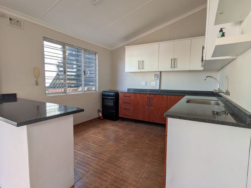 A functional kitchen featuring built-in cabinetry, granite countertops, a stainless steel sink, and tiled flooring, offering a clean and practical workspace.