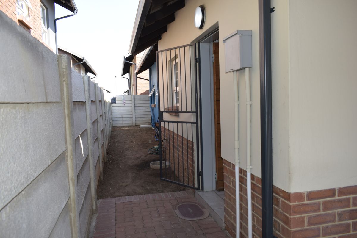A side passage of the property featuring brick paving, a security gate, and a precast concrete boundary wall.
