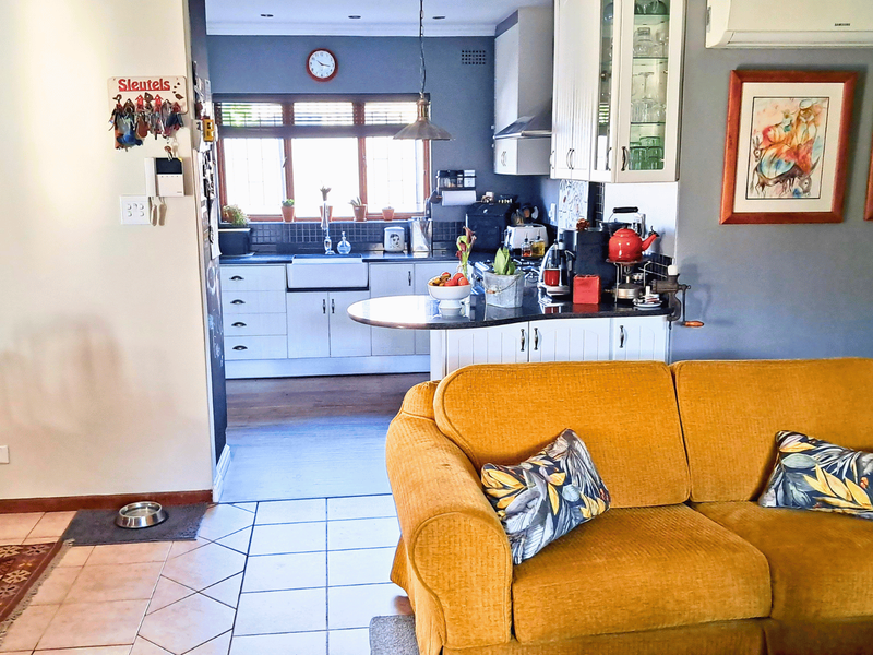 Open plan living area featuring a kitchen with farmhouse sink and granite countertops, seamlessly connected to a comfortable lounge space with air conditioning.