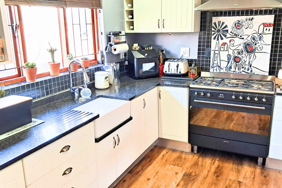 A well-maintained kitchen featuring a farmhouse sink, granite countertops, tiled backsplash, and a professional-style gas range with an integrated extractor fan.