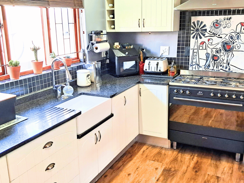 A well-maintained kitchen featuring a farmhouse sink, granite countertops, tiled backsplash, and a professional-style gas range with an integrated extractor fan.