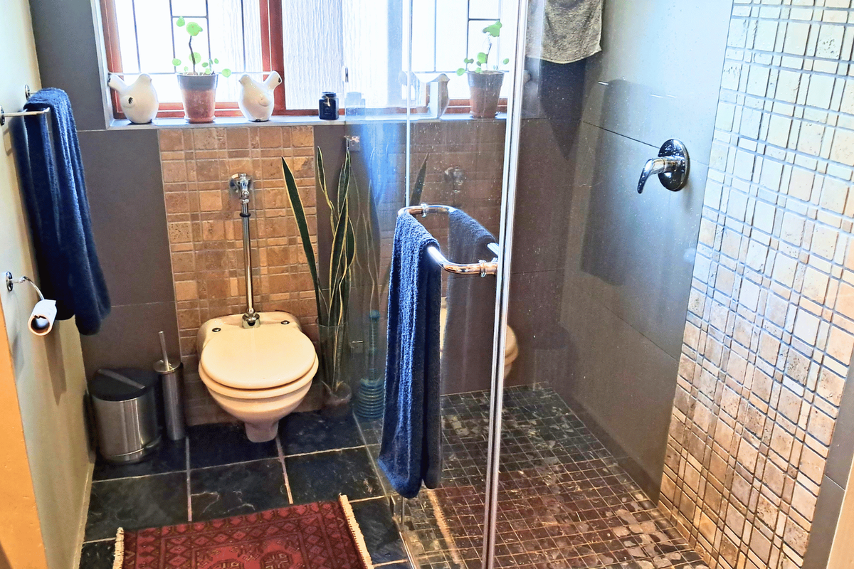 A compact bathroom featuring a glass-enclosed shower, wall-mounted toilet, and decorative mosaic tile accents, providing a functional space with potential for modern updates.