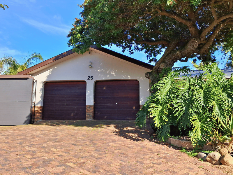 Front elevation of the property featuring a double garage with dark wood-finish doors, a paved driveway, and established garden landscaping.