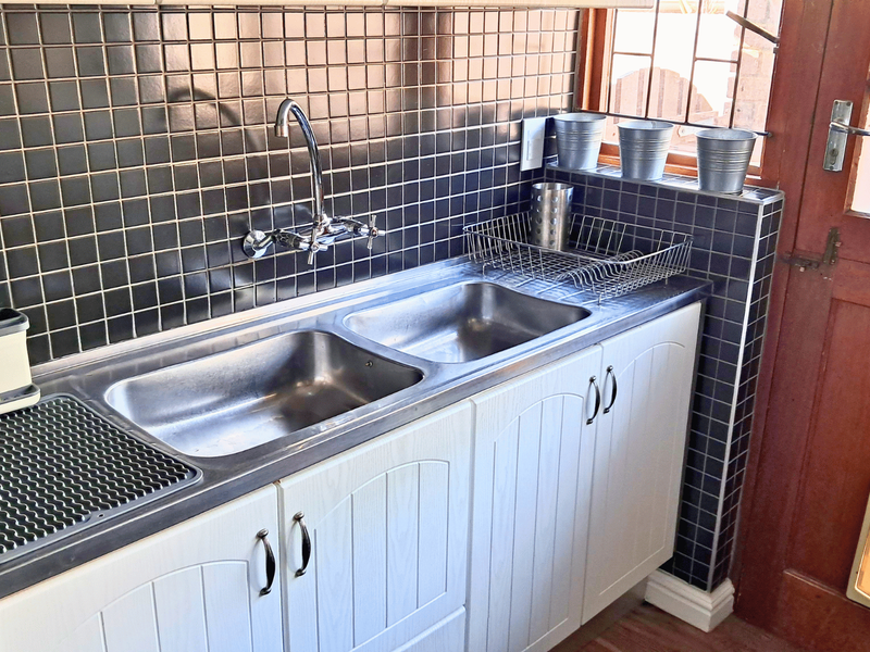 A functional scullery area featuring a double stainless steel sink, chrome mixer tap, dark tiled splashback, and white built-in cabinetry with direct exterior access.