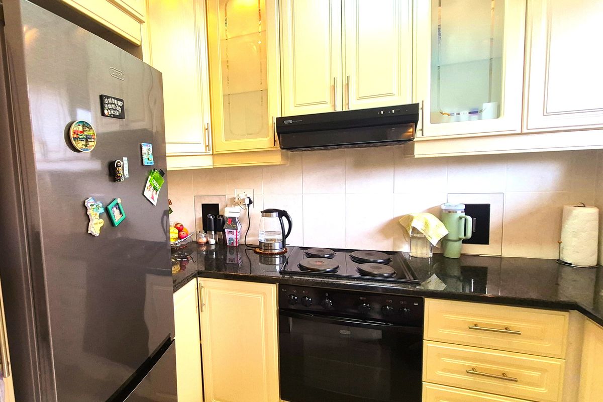 A functional kitchen featuring cream-colored cabinetry, dark granite countertops, a built-in oven, electric hob, and an extractor fan with a tiled backsplash.
