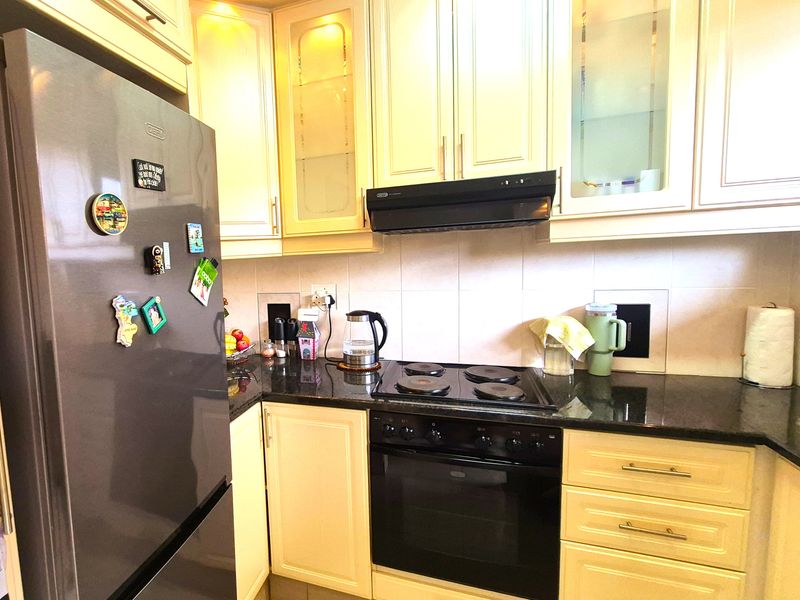 A functional kitchen featuring cream-colored cabinetry, dark granite countertops, a built-in oven, electric hob, and an extractor fan with a tiled backsplash.