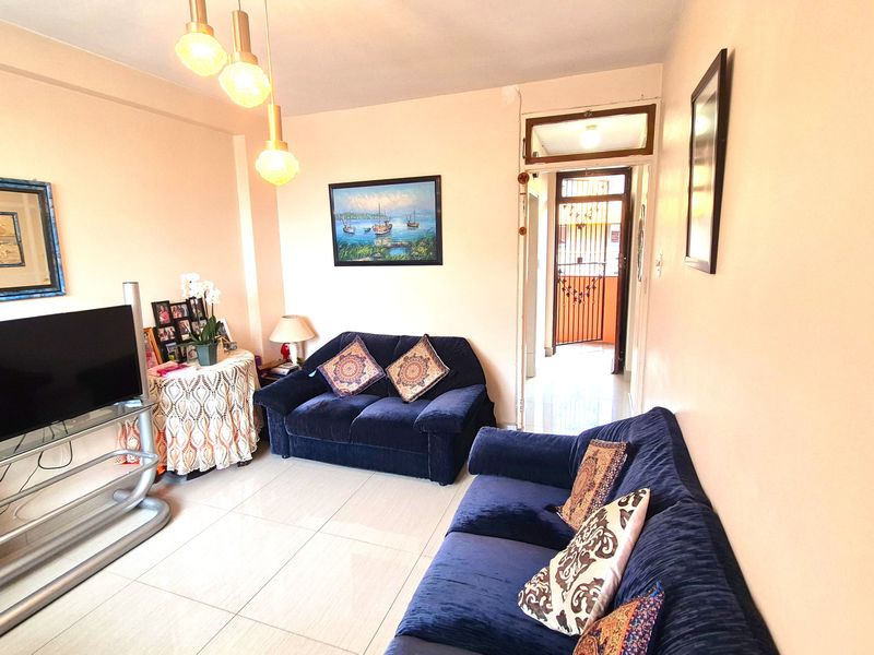 A comfortable living room featuring tiled flooring and modern pendant lighting, with a clear view leading toward the apartment entrance and security gate.