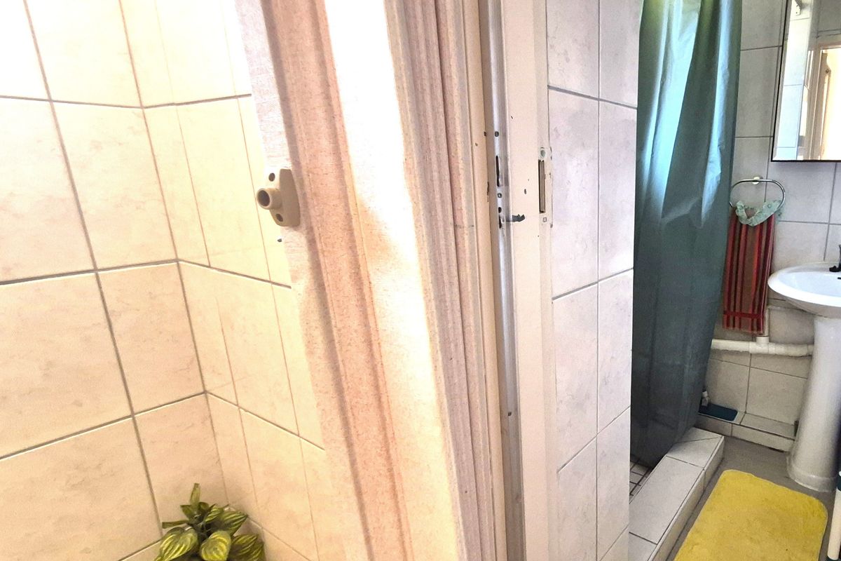 A functional bathroom featuring a pedestal basin and tiled shower area, showing signs of wear on the door frame and finishes.