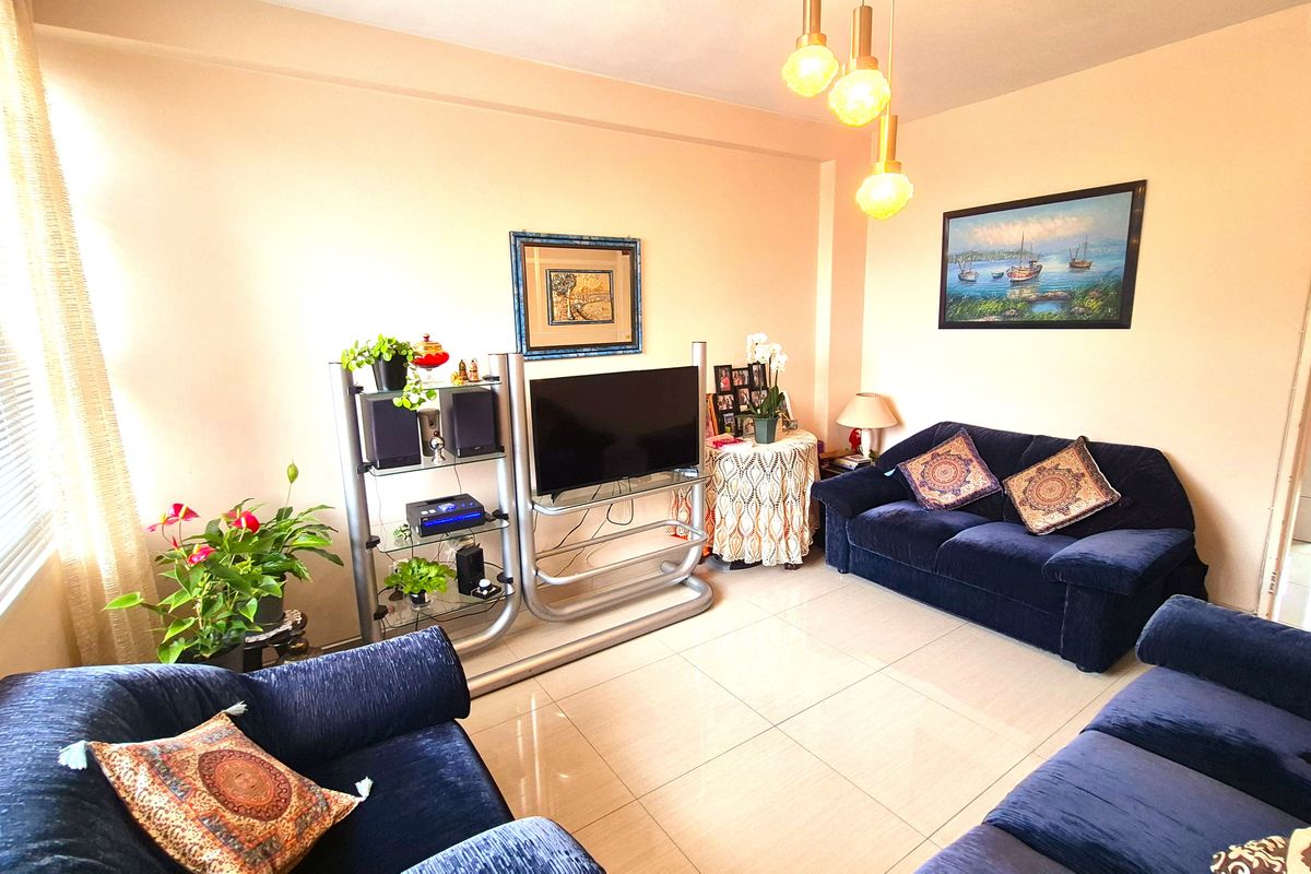 A comfortable living room featuring neutral tiled flooring, warm pendant lighting, and large windows allowing for natural light.