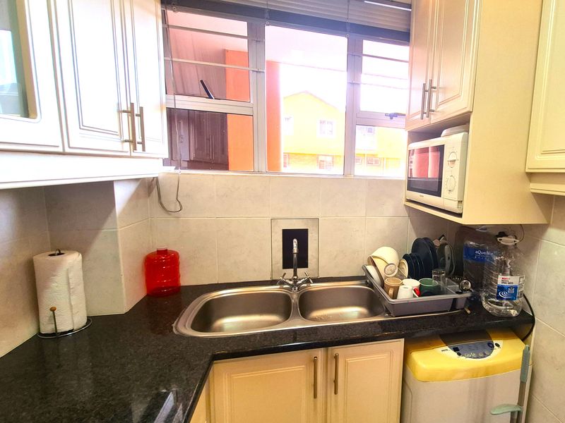 A compact kitchen featuring granite countertops, double bowl stainless steel sink, built-in cabinetry, and a tiled backsplash with a window for natural light.