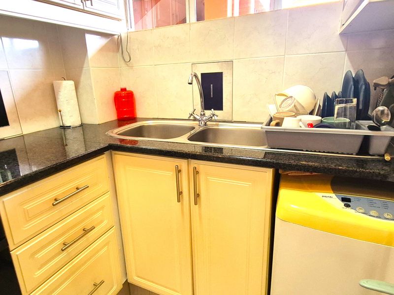 Compact kitchen area featuring granite countertops, double stainless steel sink, and shaker-style cabinetry with a tiled backsplash.