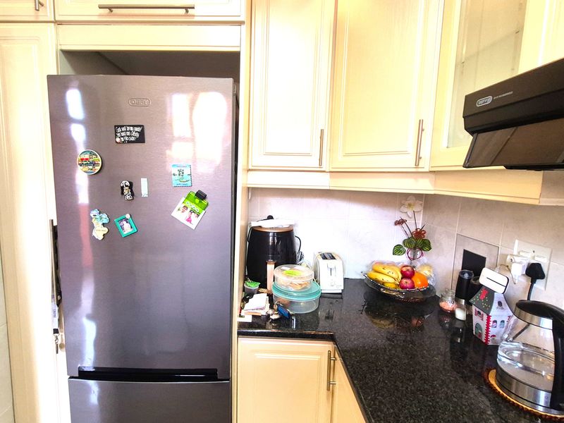 A functional kitchen area featuring granite countertops, built-in cabinetry, and a wall-mounted extractor fan with a tiled backsplash.