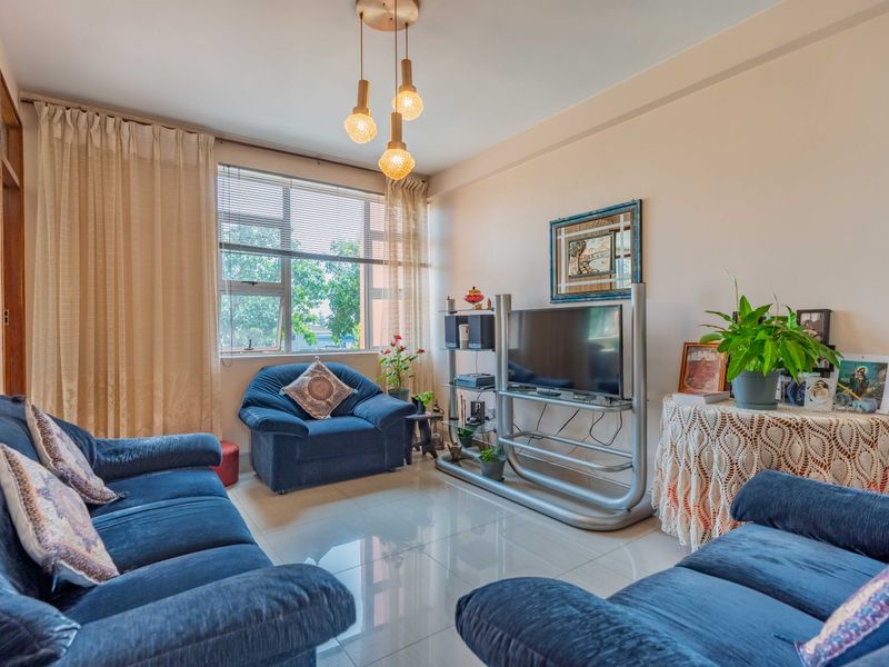 A well-lit living room featuring polished tiled flooring, a large window with natural light, and modern pendant lighting.