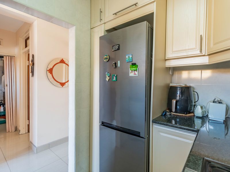 A functional kitchen area featuring built-in cabinetry, granite countertops, and tiled finishes, with a clear view into the adjacent hallway and bathroom.