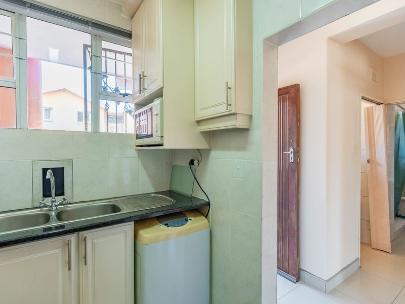 Compact kitchen featuring granite countertops, double bowl sink, and built-in cabinetry, with an adjacent view into the bathroom area.