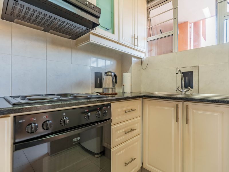 A functional kitchen featuring cream-colored cabinetry, granite countertops, a built-in electric stove with extractor fan, and a stainless steel sink with tiled backsplash.