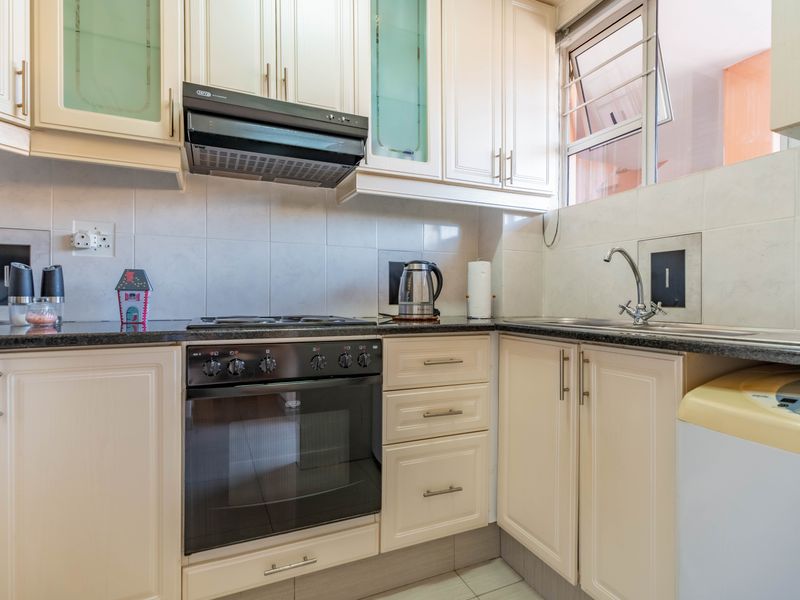 A functional kitchen featuring cream-colored cabinetry, granite countertops, a built-in oven with hob, and a stainless steel sink with tiled backsplash.