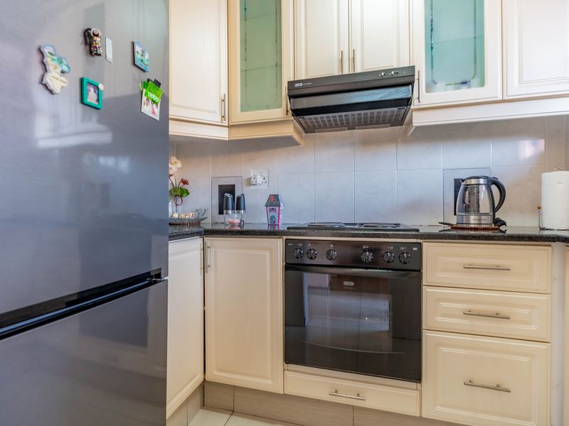 A well-maintained kitchen featuring cream-colored cabinetry, granite countertops, a built-in oven, and a hob with an extractor fan.