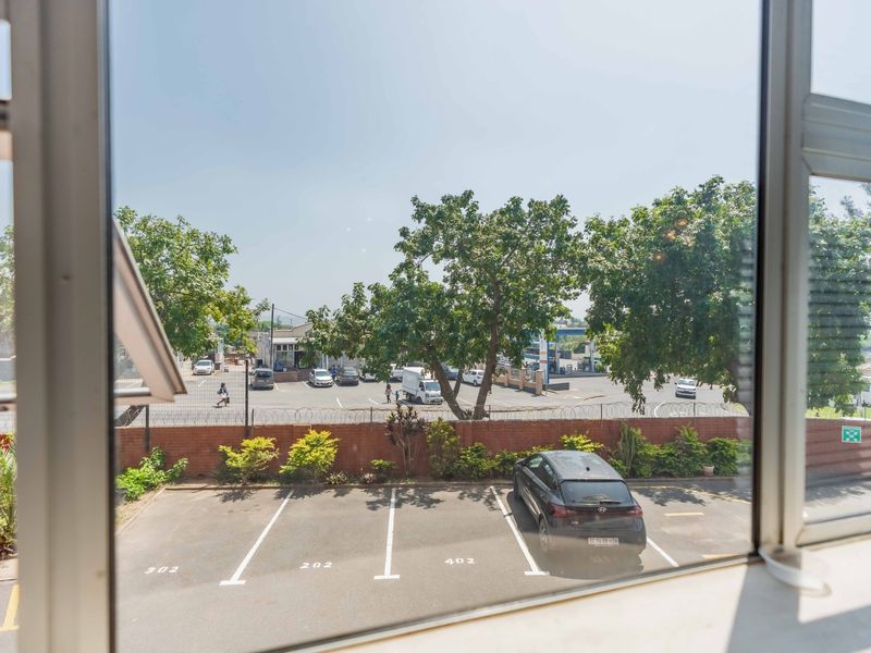 A view from an interior window overlooking a paved parking area, perimeter security fencing, and surrounding neighbourhood.