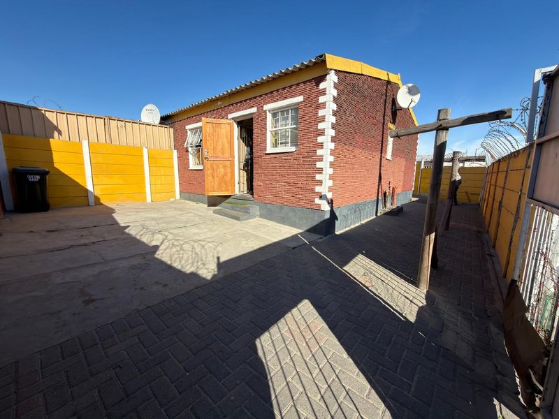 Rear exterior view of the townhouse featuring a paved courtyard, precast boundary walls with security fencing, and a satellite dish installation.