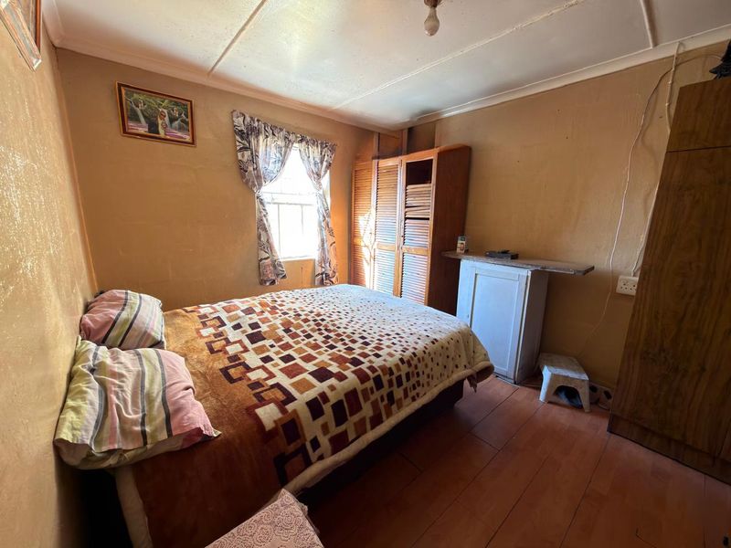 A compact bedroom featuring timber flooring, built-in wardrobe storage, and a window with natural light. The room requires cosmetic updates to improve its overall condition.