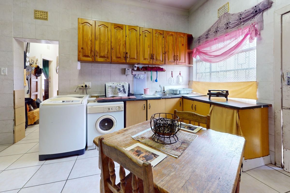 A dated kitchen featuring wooden cabinetry, tiled walls, and a functional layout with space for laundry appliances.