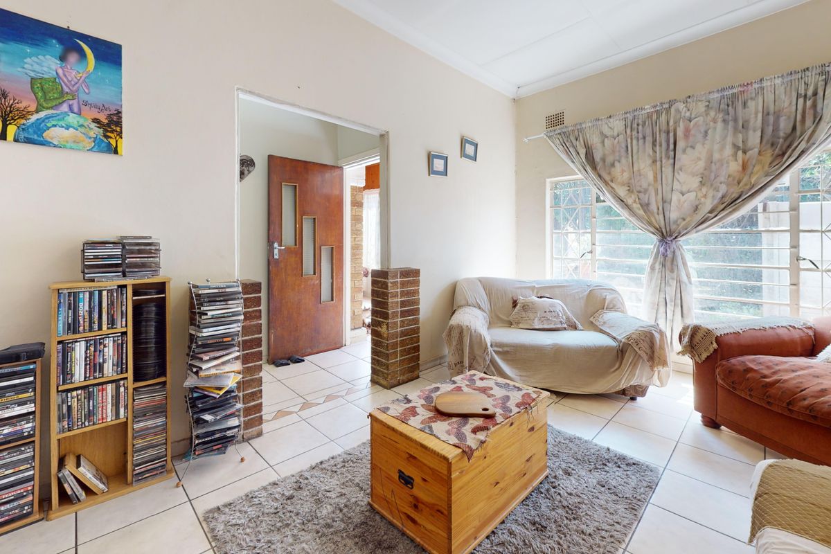 A living room featuring tiled flooring, a brick pillar accent, and a window with security bars, providing a functional space with potential for modernization.