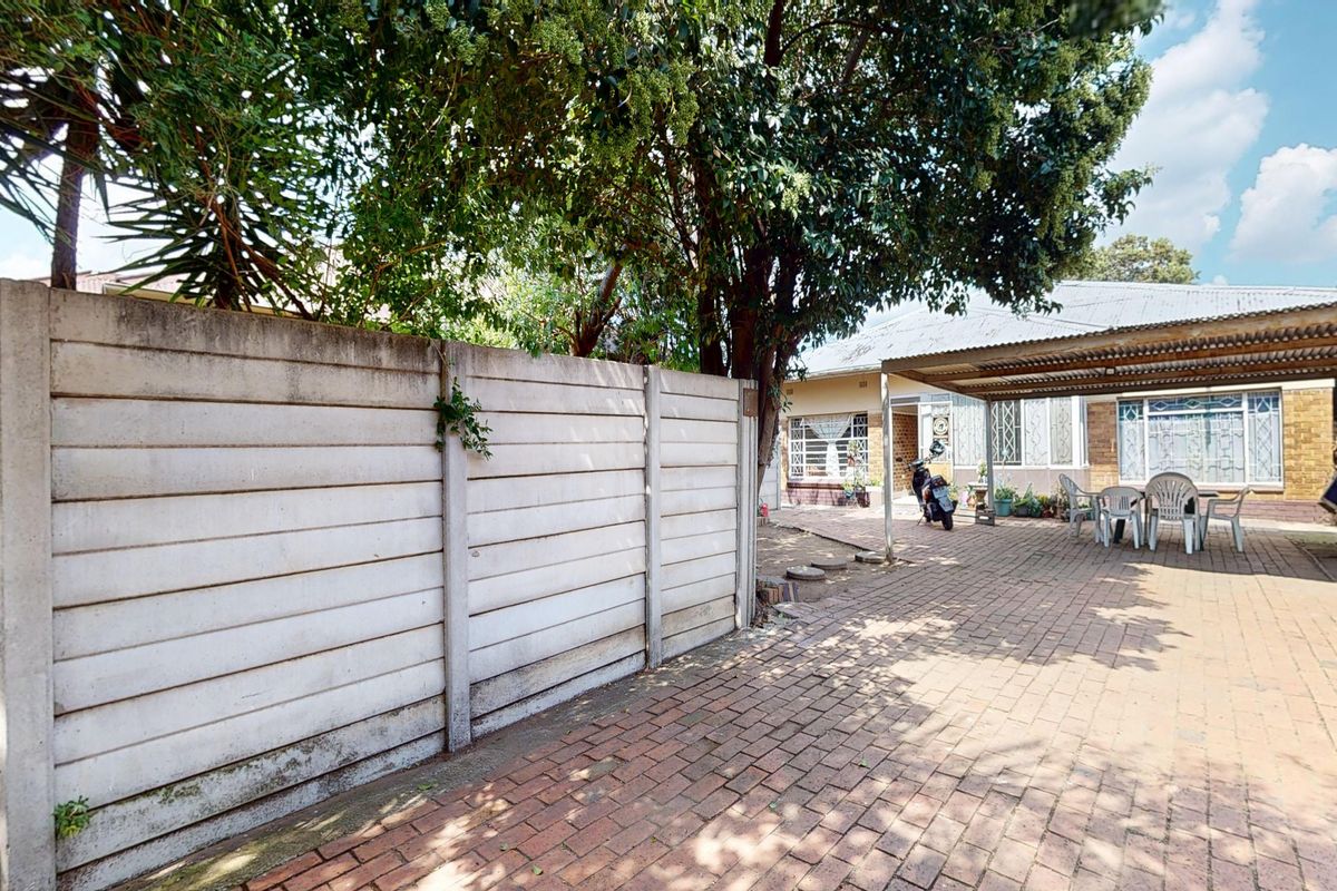 Rear exterior area featuring a paved courtyard, a corrugated metal carport, and a precast concrete boundary wall.