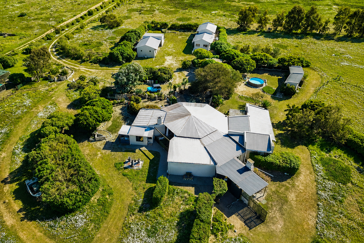 Aerial view of a small holding property featuring a main residence with a metal roof, multiple outbuildings, a swimming pool, and expansive surrounding grounds.