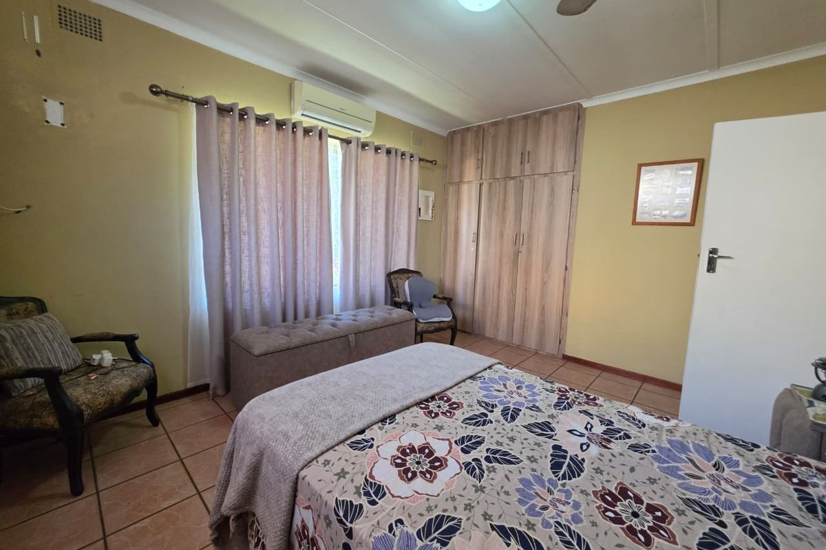 A functional bedroom featuring tiled flooring, built-in wooden cupboards, a ceiling fan, and a wall-mounted air conditioning unit.