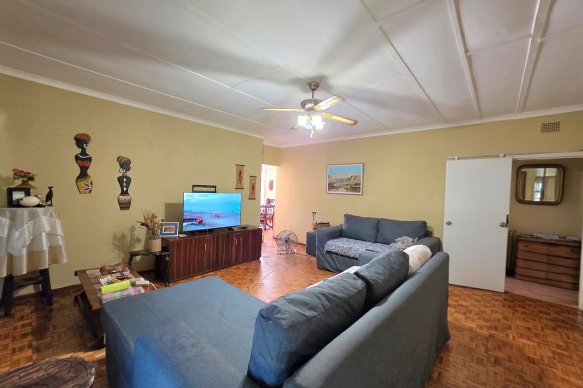 A spacious living room featuring classic parquet flooring, a ceiling fan, and a sliding door leading to adjacent areas.