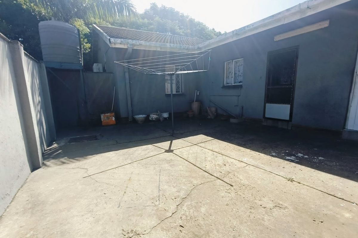 A rear exterior courtyard area featuring concrete paving, a water storage tank, and security features on the windows and door.