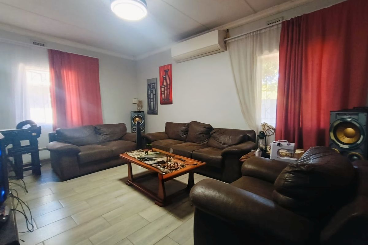 A comfortable living room featuring tiled flooring, a wall-mounted split-system air conditioner, and dual window treatments.