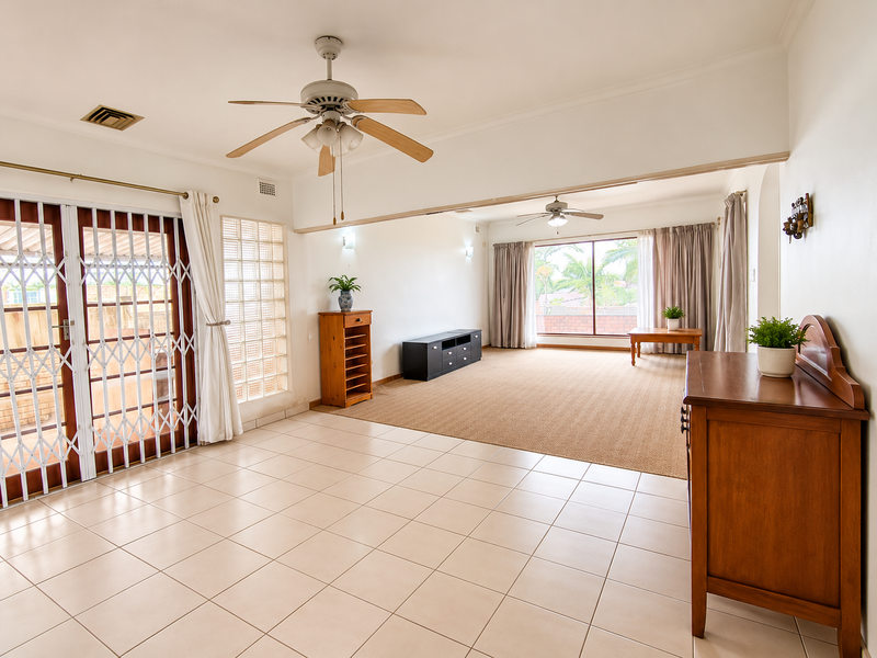 Spacious open-plan living area featuring a combination of tiled and carpeted flooring, ceiling fans, and large sliding doors leading to the exterior.