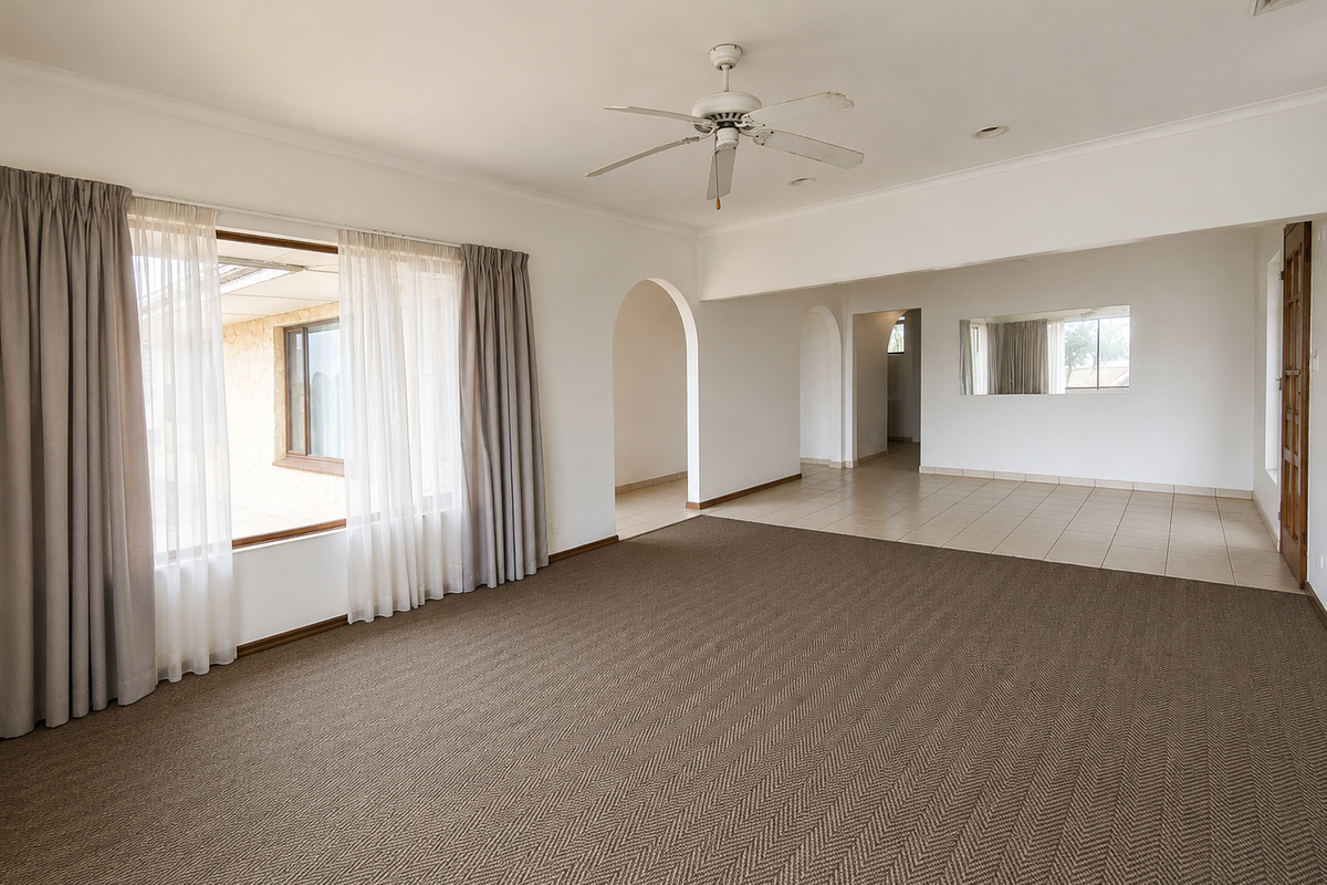 Spacious, light-filled living area featuring a combination of carpet and tile flooring, ceiling fan, and elegant archways leading to adjacent spaces.