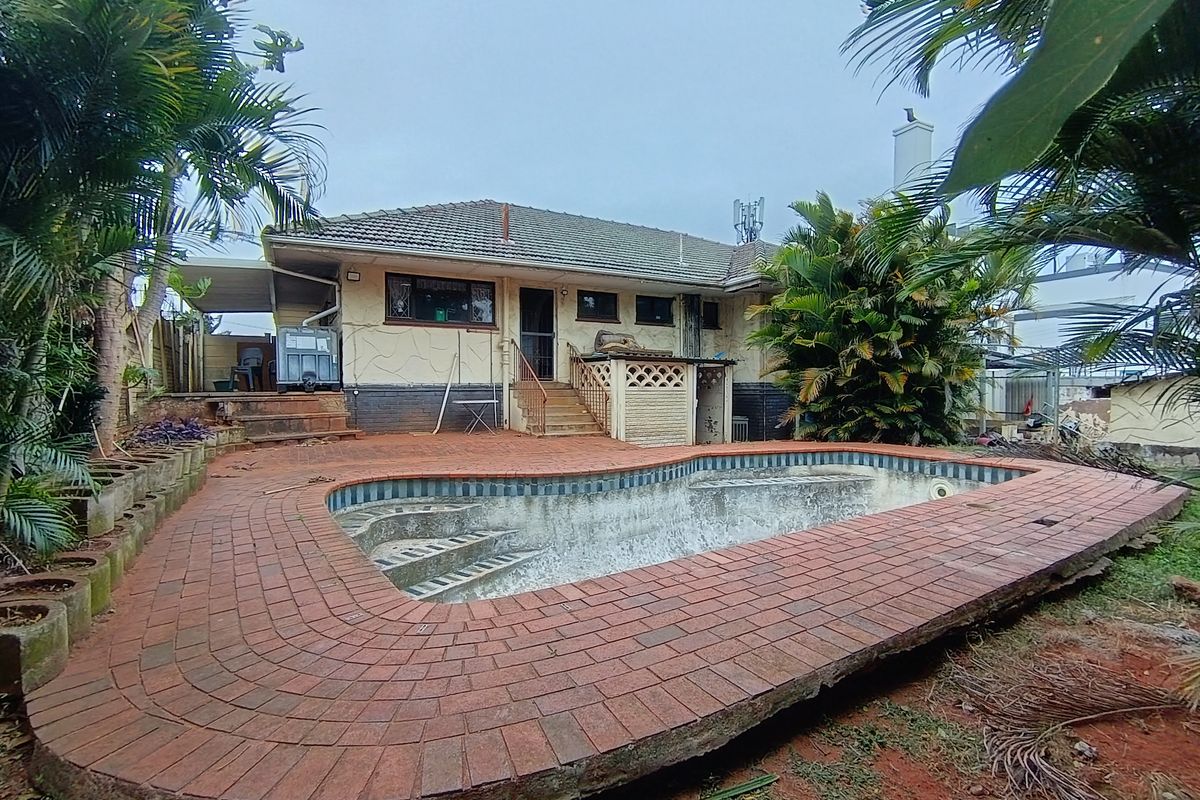 Rear exterior view featuring a swimming pool with brick paving and a single-story house structure with a tiled roof.