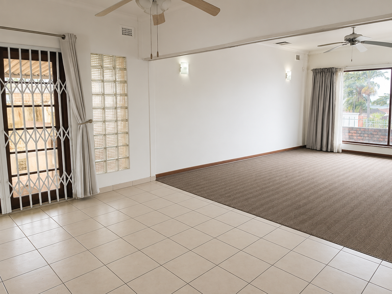 Spacious, empty living area featuring a mix of tiled and carpeted flooring, ceiling fans, and a decorative glass block feature wall.