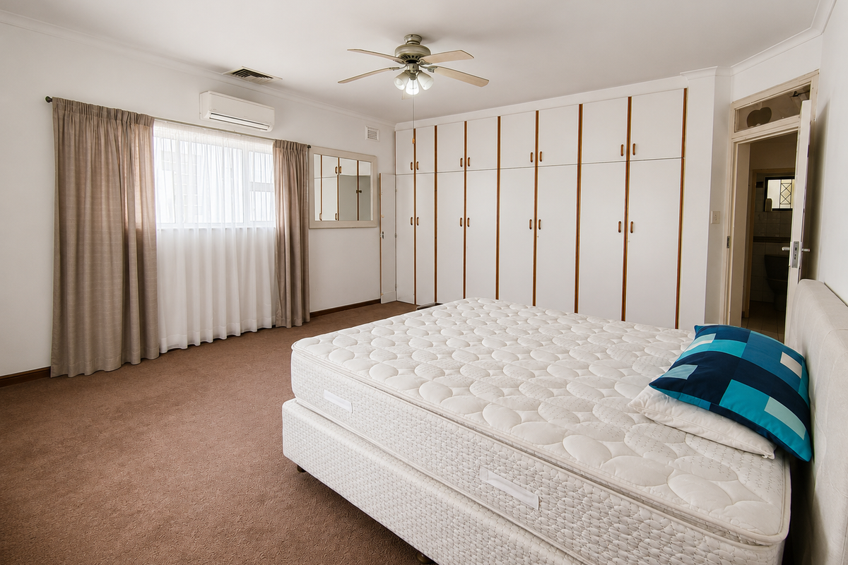 Spacious bedroom featuring extensive built-in cabinetry, carpeted flooring, a ceiling fan, and a wall-mounted air conditioning unit with an adjoining en-suite bathroom.