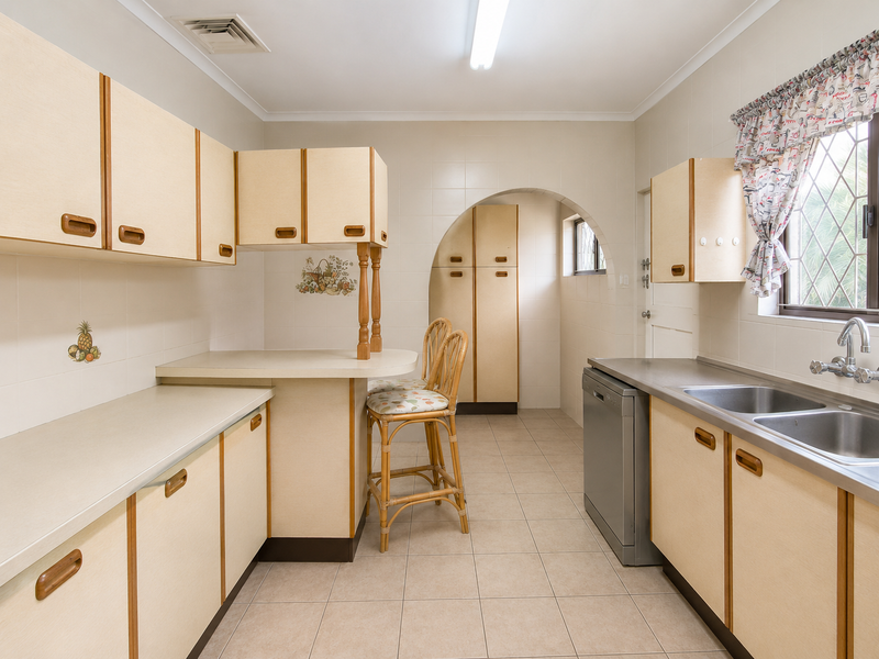 A functional kitchen featuring dated laminate cabinetry, tiled walls, ceramic flooring, and a double bowl stainless steel sink with a breakfast bar area.