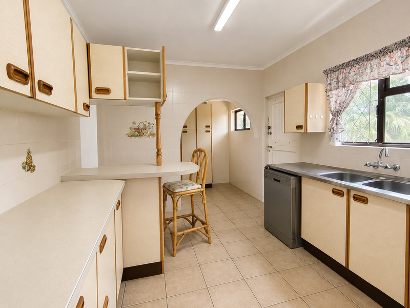 A functional kitchen featuring laminate cabinetry, tiled walls, and a double bowl stainless steel sink, offering a classic layout with potential for modern updates.
