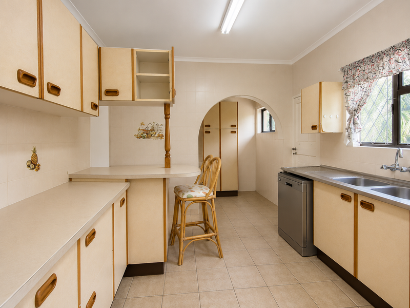 A functional kitchen featuring laminate cabinetry, tiled surfaces, and a double bowl sink, offering a classic layout with potential for modern updates.