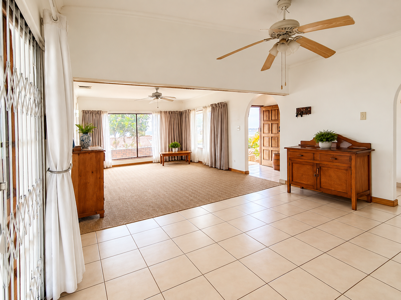Spacious living area featuring tiled and carpeted flooring, ceiling fans, and an open-plan layout with access to the exterior through a security gate.