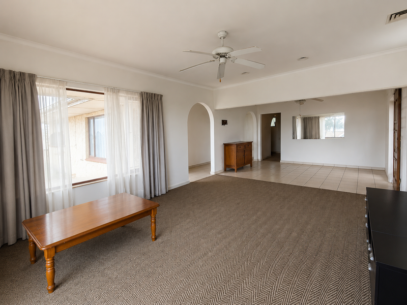 Spacious living area featuring neutral tones, an archway transition, ceiling fan, and a combination of carpet and tiled flooring.