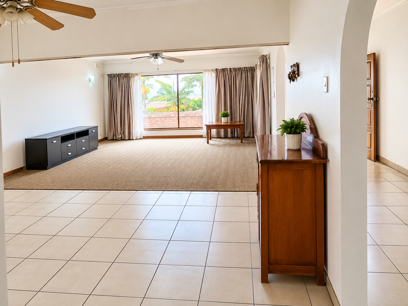 Spacious living area featuring a combination of tiled and carpeted flooring, an arched entryway, and a large sliding glass door with garden views.