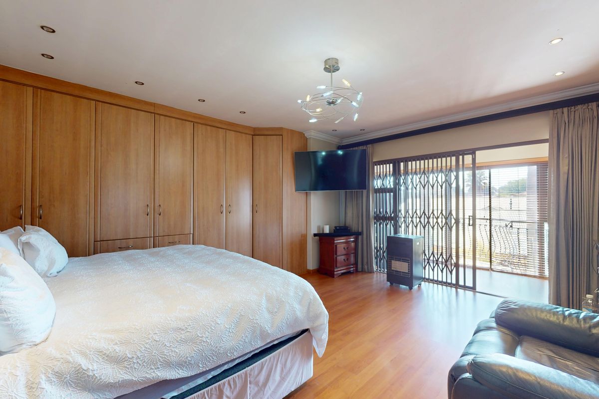 Spacious bedroom featuring extensive built-in wooden cabinetry, laminate flooring, recessed lighting, and direct access to a balcony through a secure sliding door.