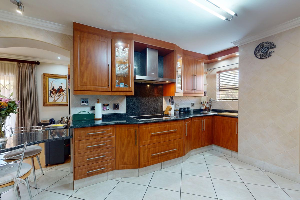A well-maintained kitchen featuring warm wooden cabinetry, granite countertops, a built-in wine rack, and tiled flooring with a functional layout.