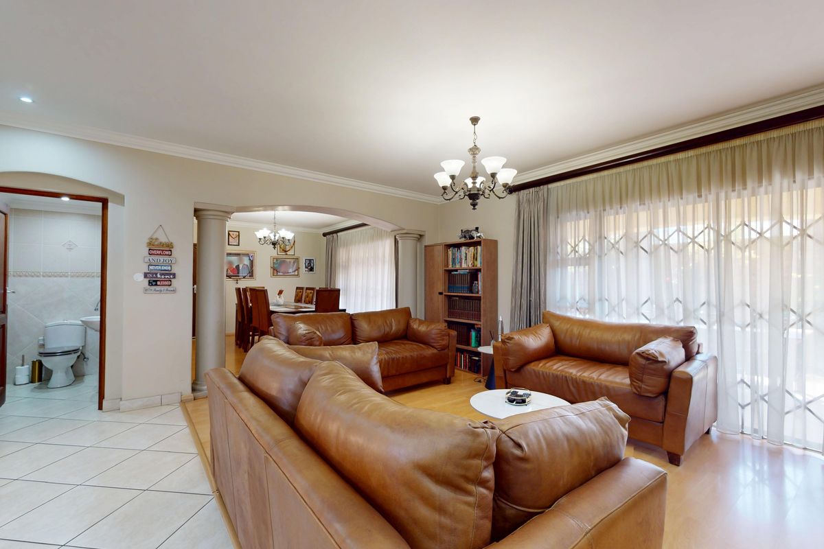Spacious living room featuring laminate flooring, decorative columns, and an open-plan flow leading to a dining area and adjacent bathroom.