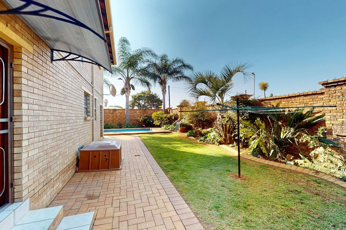 Rear garden area featuring a paved walkway, swimming pool, and brick boundary walls, providing a private outdoor space.